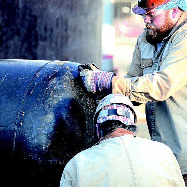 Two men with hard hats and gloves working on machine
