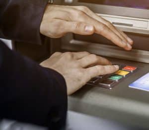 Man at ATM covering buttons while typing in PIN