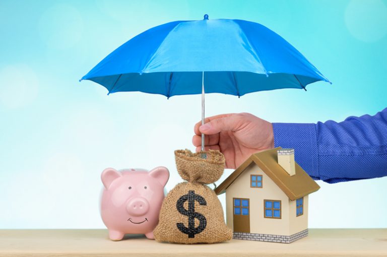 Hand holding umbrella above piggy bank, money bag, and house