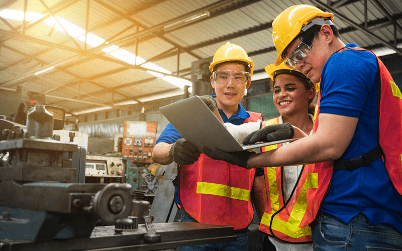 Three workers in safety hats and vests reading blueprints