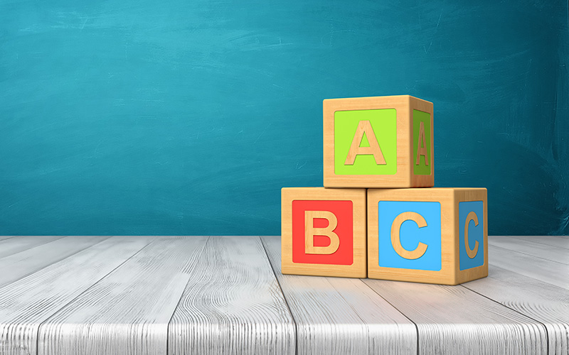 ABC blocks stacked on each other in front of teal background with woodgrain table