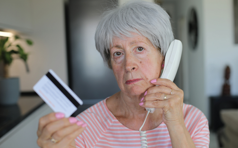 Elderly women on a hand held phone with a scammer on the other line while holding a credit card