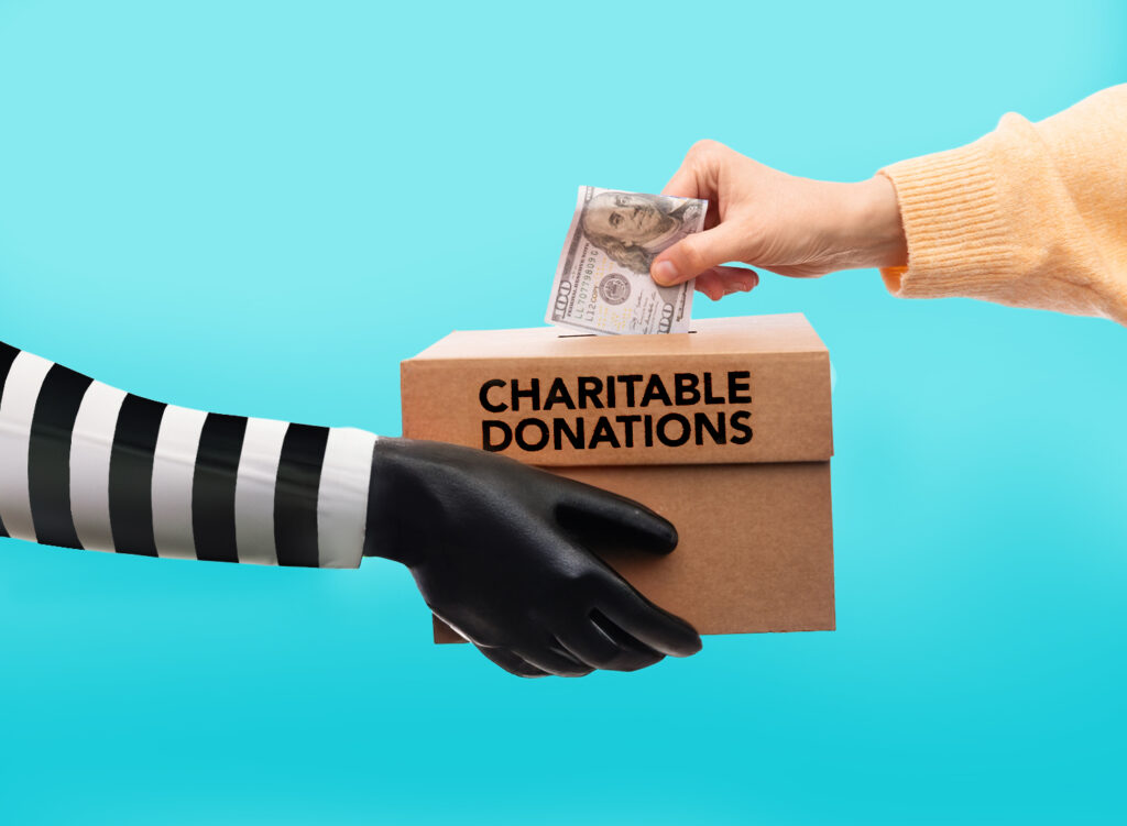 A person puts cash into a box labeled "Charitable Donations" held by a gloved hand in a striped sleeve against a blue background.